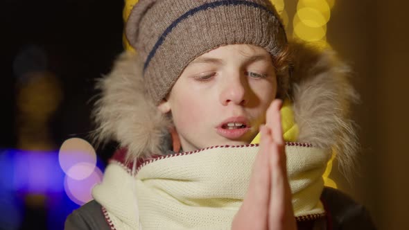 Closeup of Freezed Caucasian Boy Warming Hand Rubbing Palms and Blowing Outdoors in City