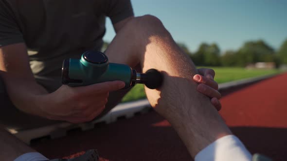 Athletic Male Massages Muscles with Hand Massage Gun Recovering From Stadium Running Workout