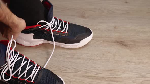 Close-up of a man putting on basketball sneakers and tying his laces. Side view from above