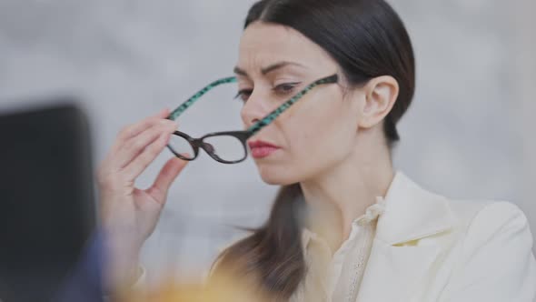 Portrait of Exhausted Young Female Employee or CEO Taking Off Eyeglasses Rubbing Nose and Continues