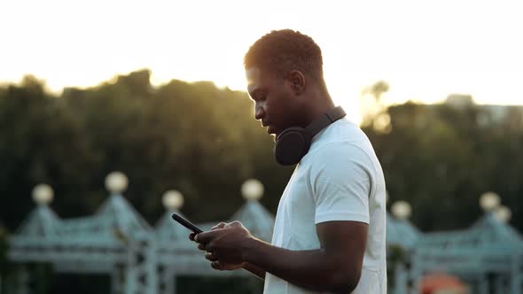 Black Man Looks at Smartphone Screen at Back Sunlight