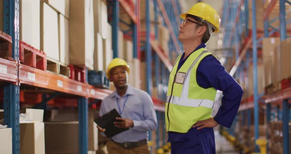 Diverse male workers wearing helmet and touching back in warehouse