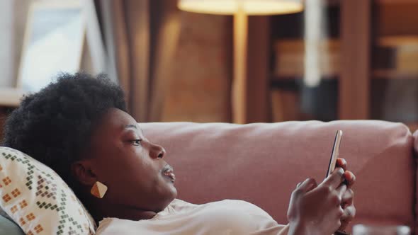 African American Woman Lying on Couch and Using Smartphone