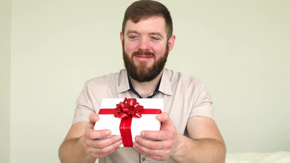 Smiling bearded man presenting gift box. Birthday and Valentines Day concept.