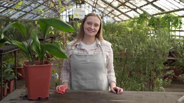 Young Woman Stands Near Large Table with Green Flowers on It and Smiles