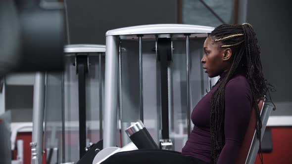 A Black Woman with Braids Training Her Legs on a Exercise Equipment