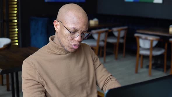 African American Man with Freckles on His Face Types Text on a Laptop Keyboard