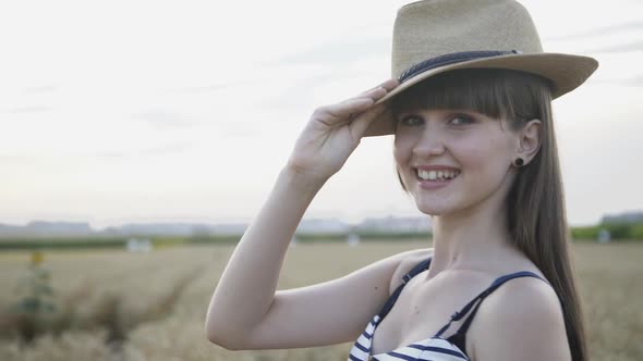 Portrait of Seductive Girl Puts on Hat and Looks at Camera with Smile