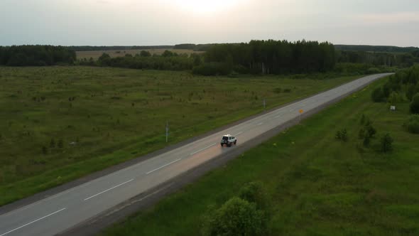 Aerial View of a Car Driving Along the Road Among Fields of Green Grass