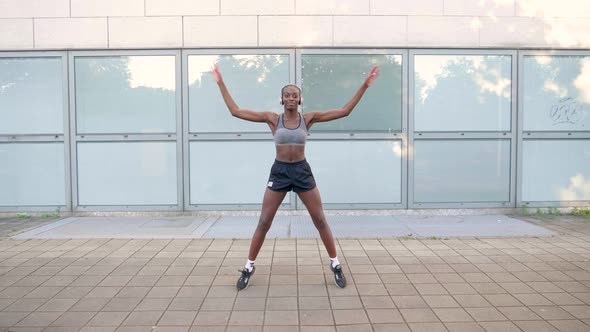 Slow motion shot of young woman with headphones jumping jack in city