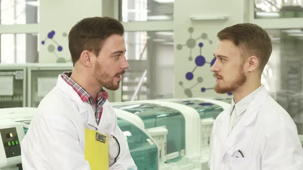 Two Young Lab Technicians Stand in the Middle of the Laboratory and Talk