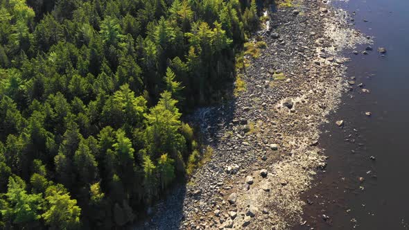 Early fall aerial footage of remote lake in northern Maine orbiting close around rocky wooded shorel