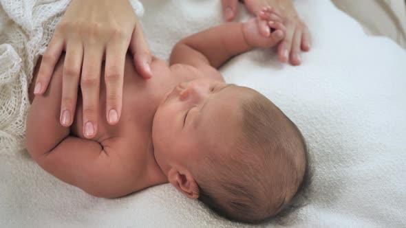 Close up of mother hands lulling newborn baby on bed at home