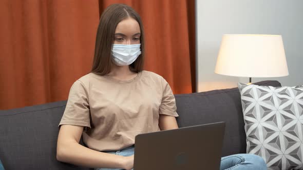 Young Woman with Protective Mask Working From Home and Using Laptop at Sofa