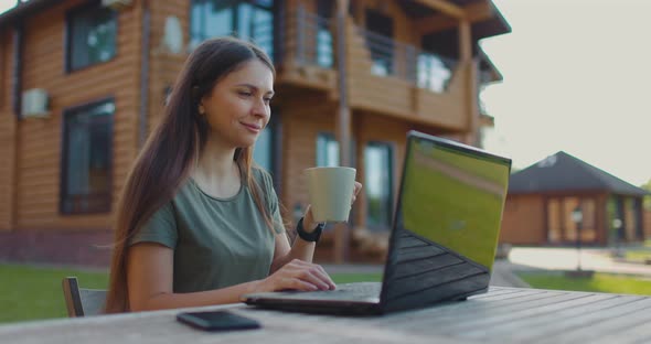 Young Woman Working with Laptop at Table on Plot of Country House