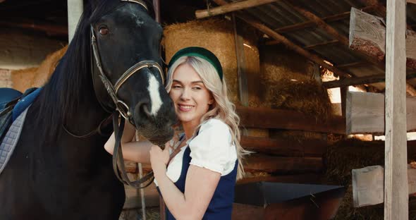 Blonde Smiling and Caressing a Cute Black Horse's Head at Camera at Stable