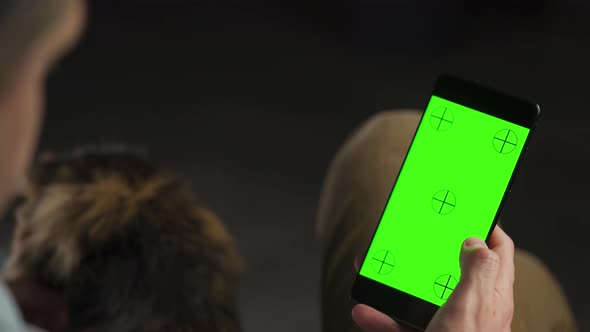 Man Using Smartphone with Green Mockup Screen in Vertical Mode and Stroking Cat