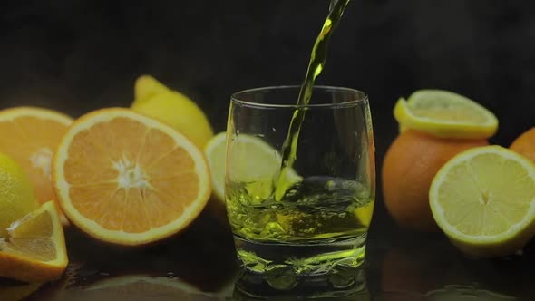 Pour Juice Into Glass, Orange and Lemon Slices on Background. Slow Motion