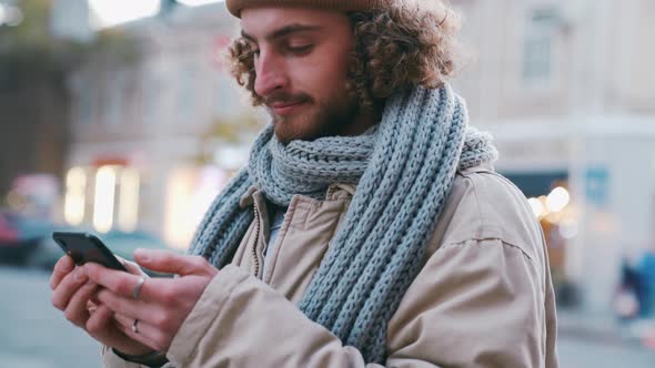 Handsome curly-haired man texting by phone