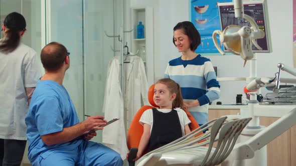 Friendly Man Dentist Assistant Interrogating Kid Patient