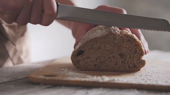 Male hands cut slice crispy bread. Fresh homemade whole grain bread. Bamboo cutting board on table