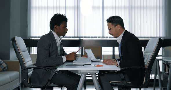 Two Young Businessman Talking at Desk in Office