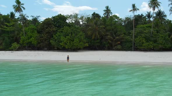 Aerial slow motion: Woman relaxing in turquoise water white sand beach tropical