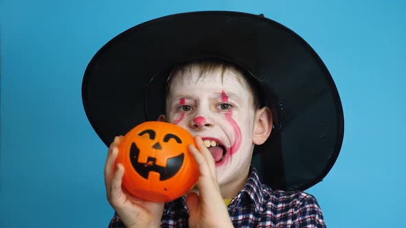 Caucasian boy 8 years old in a hat with make-up on his face holds a pumpkin for Halloween day.Childr