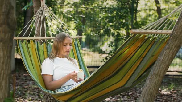 Young Woman is Having a Rest Lying in Colorful Hammock and Eating Tasty Ice Cream