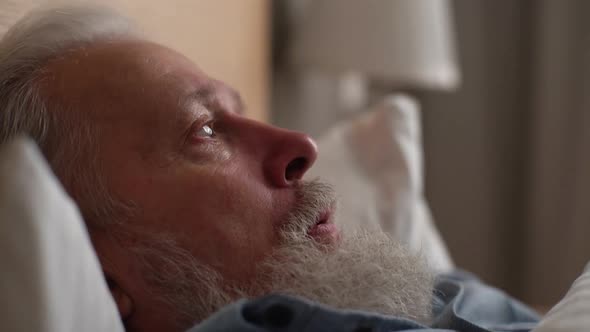 Closeup Face of Sick Sad Grayhaired Senior Adult Male Writhing in Pain Talking to Doctor Lying on