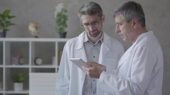 Two Male Doctors Checking Information on the Tablet, Discussing