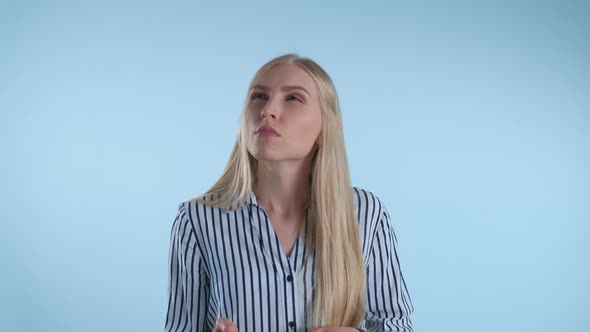 Blonde Young Woman Holding Her Chin with Hand While Thinking About Something on Blue Background