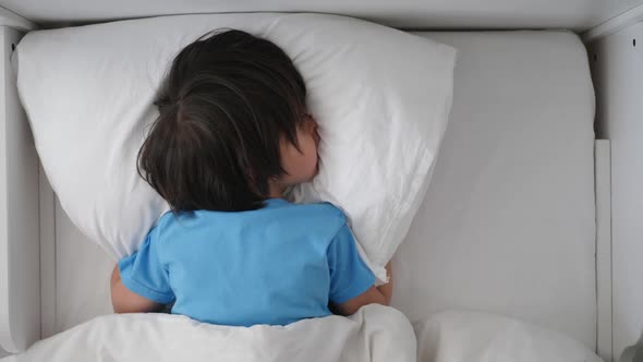 Boy Child in a Blue Tshirt Lies on a White Bed