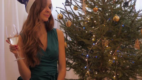 Woman with Champagne Glass Sits Against Christmas Tree