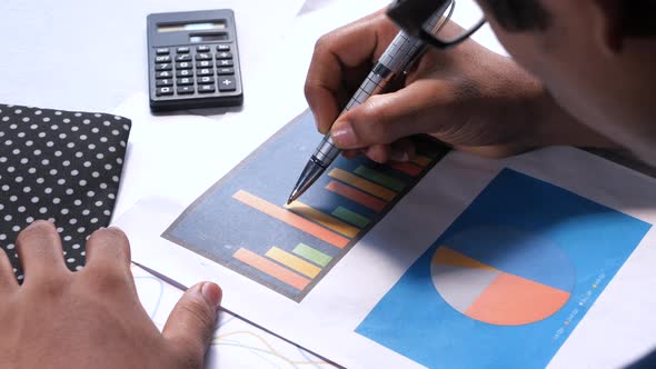 Rear View of Man's Hand Analyzing Bar Chart on Paper 
