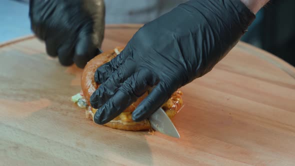 Chef Cutting Tasty Burger with Knife on Wooden Board