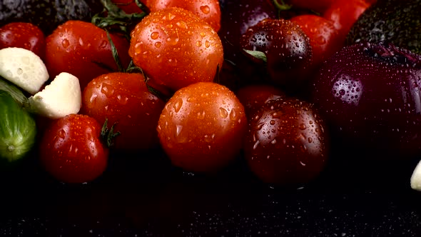 Cherry tomatoes, cucumbers, garlic, avocado and red onion on a black background in water drops.