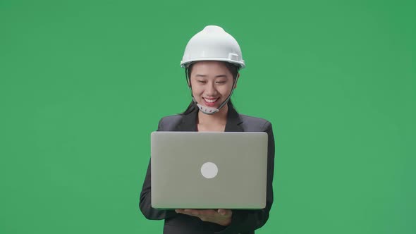 Smiling Asian Female Engineer With Safety Helmet Using A Laptop In The Green Screen Studio
