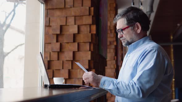 Senior Man Studies Documents Sitting in a Cafe