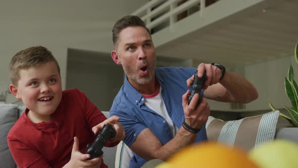 Happy caucasian father with son sitting in living room and playing video games