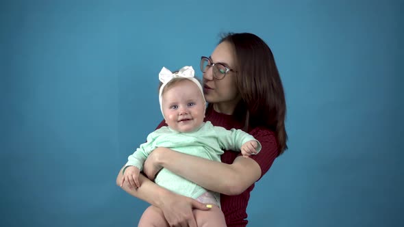 A Young Mother Holds a Baby in Her Arms. Woman with a Daughter on a Blue Background.