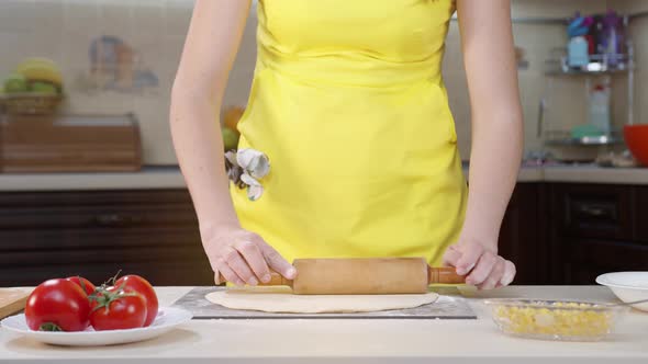 Female Chef Cooks in the Kitchen in Yellow Clothes. Female Hands Smooth the Dough on the Pizza Table
