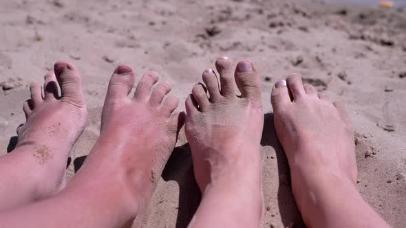 Tanned Red Bare Feet of Mother and Child in Sand Lies on a Sandy Beach