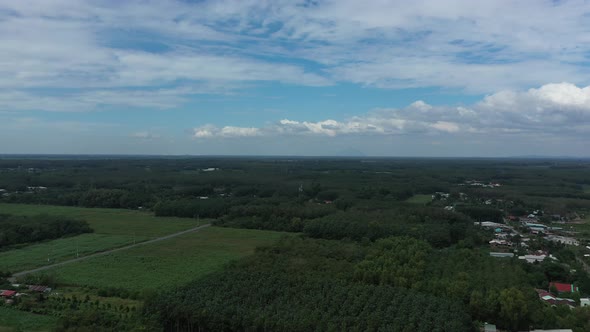 Aerial panning shot of Cu Chi, Vietnam with farms, forests on sunny day with blue sky.