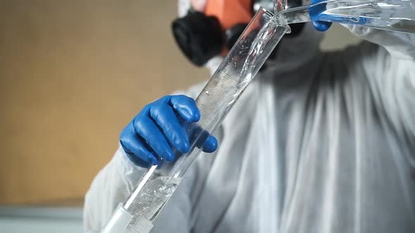 scientist biochemist in respirator in laboratory pours solution into a beaker.