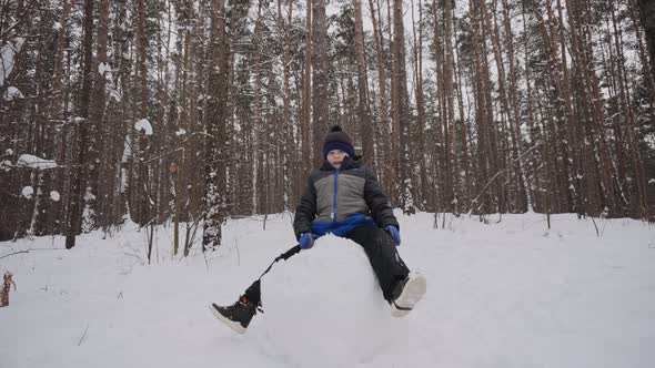 Caucasian Child From Sitting on Large Snow Ball Smiling and Knocking on Snow