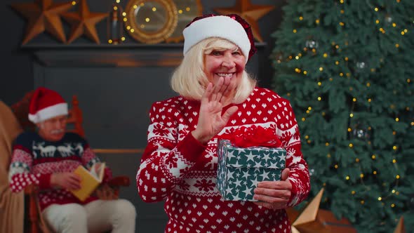 Mature Grandmother in Christmas Sweater Smiling Friendly at Camera and Waving Hands Gesturing Hello