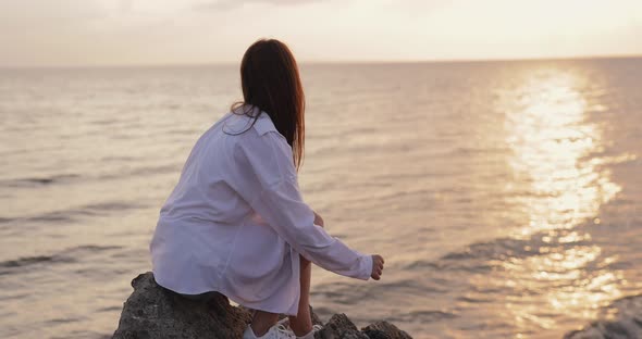 Young Woman Looks at the Sea Sunset Sitting on a Hill