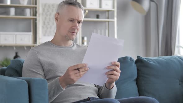Penisve Gray Hair Man Reading Agreement Sitting on Sofa