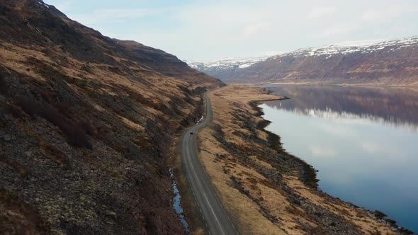 Drone Tracking Car Driving By Fjord And Towards Mountains